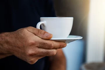 Foto op Plexiglas Close-up of man hand holding white cup of coffee or tea on black background. the mug with hot drink on a saucer © Yelena