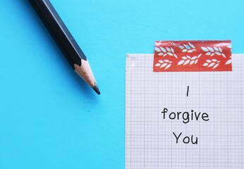Pencil and note on blue background with handwritten text I FORGIVE YOU - concept of making decision...