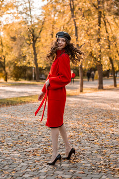 attractive stylish woman walking in park dressed in warm red coat