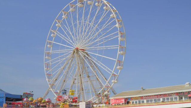 Big wheel on pier spinning in sunlight with stops and starts. Blackpool Central Pier, Lancashire, UK. Time lapse 30x.