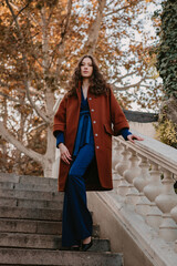 beautiful stylish woman walking in street stairs dressed in warm brown coat and blue suit