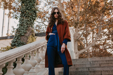 beautiful stylish woman walking in street stairs dressed in warm brown coat and blue suit