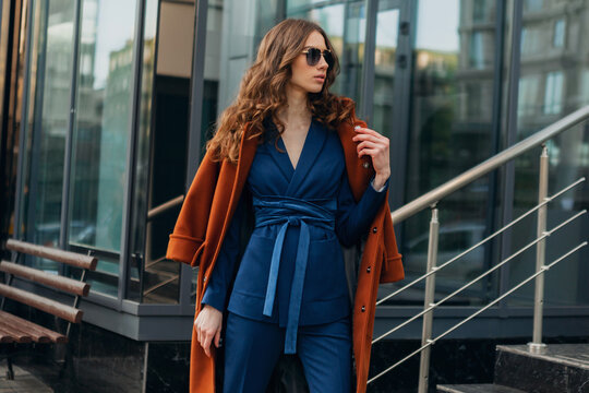 beautiful stylish woman walking in street stairs dressed in warm brown coat and blue suit