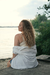 Fototapeta na wymiar sad young curly girl on the shore of a pond in summer