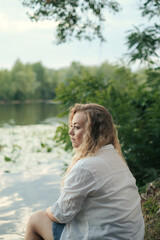 sad young curly girl on the shore of a pond in summer