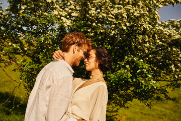 newlyweds couple in countryside, asian bride in white dress and groom hugging near big tree