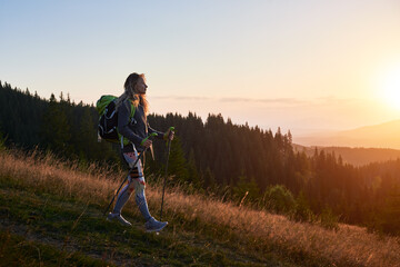 Woman tourist hiking in mountains at sunset. Sporty, positive woman traveling outdoors. Young,...