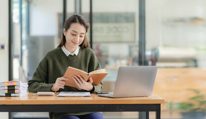 Asian businesswoman working with papers and laptop sitting at table in office, analyzing business accounting calculations and financial planning concepts.