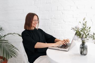 Smiling young woman in glasses holds online meeting via laptop. Businesswoman, entrepreneur,...