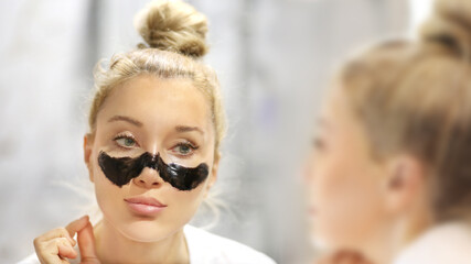 cleansing facial mask, woman looking in the mirror in the bathroom