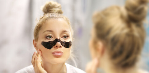 cleansing facial mask, woman looking in the mirror in the bathroom