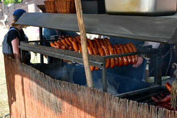 A close up on a set of various sausages and kielbasa types grilled and fried on a temporary grill made out of metal and having a small bonfire underneath seen on a sunny summer day in Poland