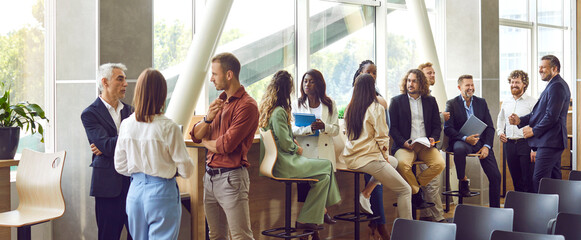 Diverse business professionals communicating at a conference, seminar or other educational event. Young and mature multiethnic people meeting in the office and having discussions. Banner background - 648103222