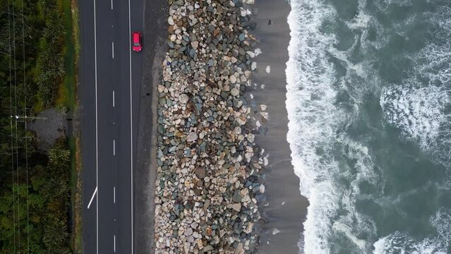 Bruce Bay, New Zealand: top down drone footage of coastal road and beach of Bruce Bay  near Haast in the New Zealand south island wild West coast on a rainy day with a red car parked