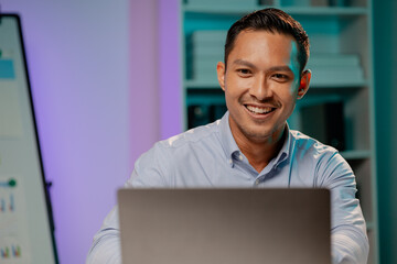 Asian man in dark office, company employee working overtime, working in the middle of the night, working overtime of a company employee who is busy and working hard. Overtime concept.