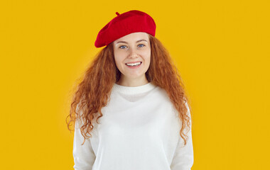 Young happy curly redhead girl with long hair wearing red beret and white knitted sweater is posing...