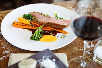 Duck fillet with sweet potato cream, roasted carrots, kale, beet-port sauce on white plate. Grilled and roasted poultry closeup served on a table for lunch in modern cuisine gourmet restaurant. - 648107673