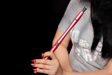 The hand of a girl with a red manicure holds a hookah pipe, a smoking object on a dark background