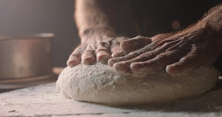 Closeup shot of hands of senior bakery chef applying flour on dough, old man kneading dough, making...