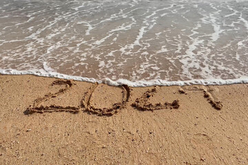 Fototapeta na wymiar Happy New Year concept. Text 2024 handwritten in sand surface. Blue ocean wave washing away numbers on beach.
