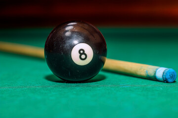 Black billiard ball number 8 and cue on a green table in close-up