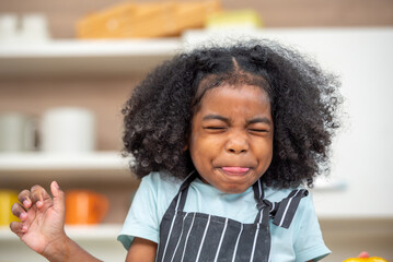 african afro hair black kid Cute taste oranges citrus sour flavour on ripe mouth in kitchen. candid...
