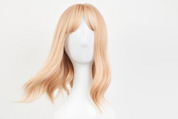 Natural looking blonde fair wig on white mannequin head. Middle length hair cut on the plastic wig holder isolated on white background, front view.