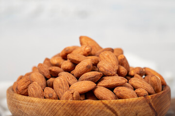 Almond in wood bowl. Roasted almonds on white wood background. Close up