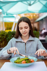 teenager girl eat fresh fish salad with knife and fork outdoors in cafe