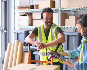 Woman Using Digital Tablet And Male Colleague With Down Syndrome In Warehouse Wearing Headsets