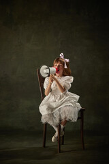 Portrait of little girl, child shouting to megaphone in white dress sitting on chair against vintage background. Fairy princess or queen. Heroine of story tale.