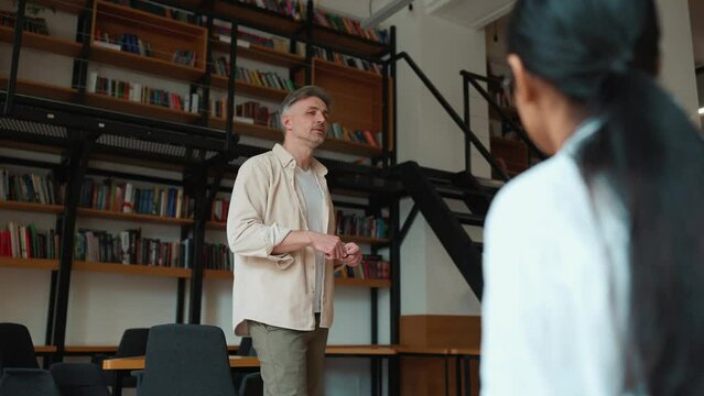 Serious grey haired male teacher agrees with a student during a lecture in the library