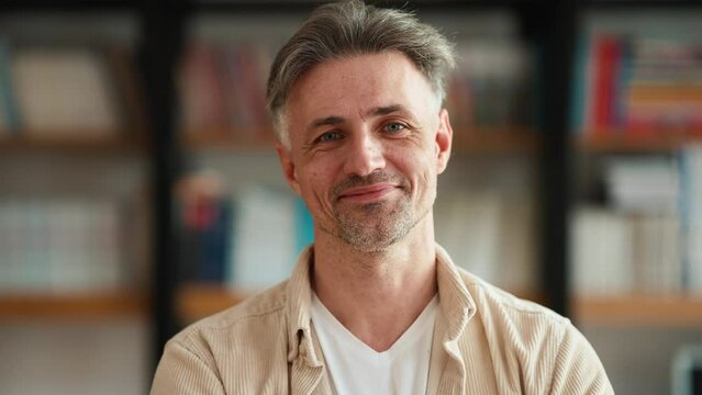 Positive Grey Haired Mature Teacher Looking At Camera In The Library