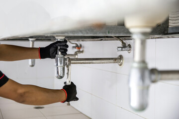 Technician plumber using a wrench to repair a water pipe under the sink. Concept of maintenance,...