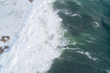 Aerial photo of a rocky shore with crashing waves creating foam.