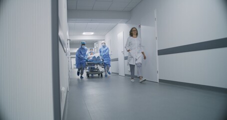 Doctors, nurses and paramedics run and push stretcher with seriously injured patient to surgery room. Medical personnel save human life in emergency department. Medical facility hallway. Slow motion.