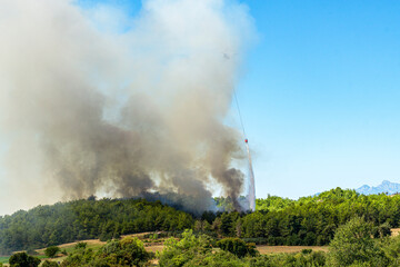 tragic view of forest fire and helibucket which  is a specialized bucket suspended on a cable carried by a helicopter to deliver water for aerial firefighting 