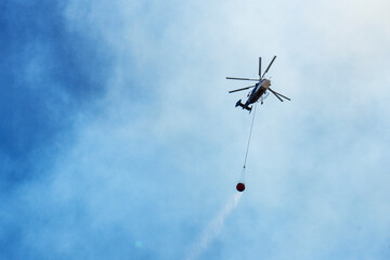 tragic view of forest fire and helibucket which  is a specialized bucket suspended on a cable carried by a helicopter to deliver water for aerial firefighting 