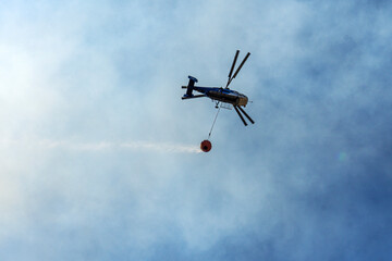 tragic view of forest fire and helibucket which  is a specialized bucket suspended on a cable carried by a helicopter to deliver water for aerial firefighting 
