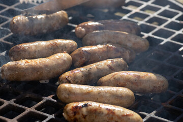 The cook prepares grilled sausages on a grill over coals outdoor.