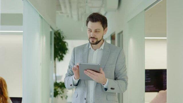 Businessman Walking in the Office Using Digital Tablet, Texting with Clients. Successful Boss Manager in Workspace Efficiently Utilizing Device for Work.
