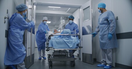 Nurse and paramedic quickly open medical facility corridor doors. Multi ethnic surgeons push stretcher with seriously injured elderly man to operating room. Medical staff work in emergency department.