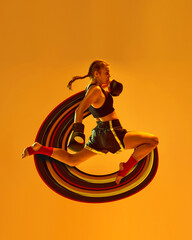 Leg kick. Sportive teen girl, mma athlete in motion, training over orange background with abstract...