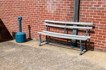 a cigarette disposal recipient and a wooden bench on a red brick wall