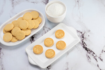 ingredients and mise en place for the preparation of cornstarch alfajores, filling the dulce de leche filling on top and grated coconut on the outside on white plates.