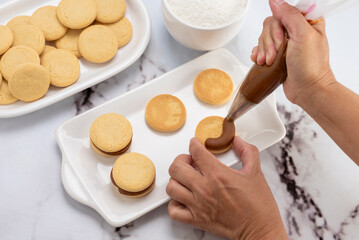ingredients and mise en place for the preparation of cornstarch alfajores, filling the dulce de leche filling on top and grated coconut on the outside on white plates.