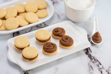 ingredients and mise en place for the preparation of cornstarch alfajores, filling the dulce de leche filling on top and grated coconut on the outside on white plates.