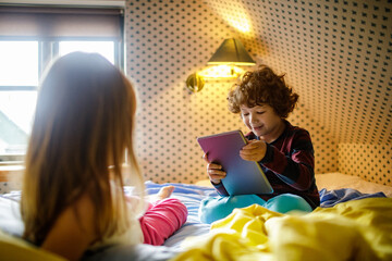 Young brother and sister using a tablet together in a bedroom