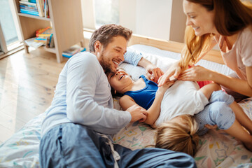 Fototapeta premium Young Caucasian family having fun and playing together in the bedroom in their pajamas