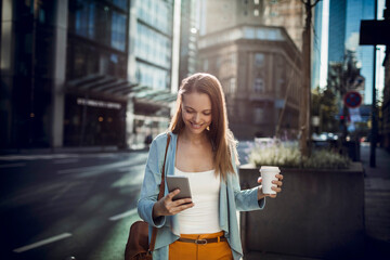 Young businesswoman using her smartphone and having coffee while commuting to work in the city